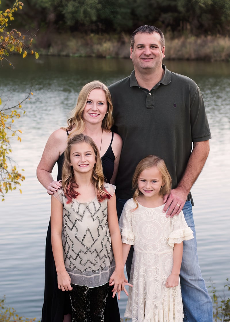 Family Photographer, family of four with two daughters stand at quiet river's edge