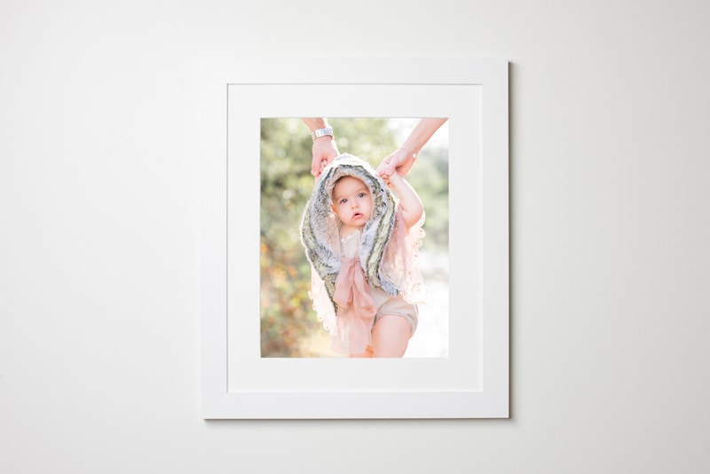 Newborn photography, a white frames picture hangs on the wall, a baby is pictured inside