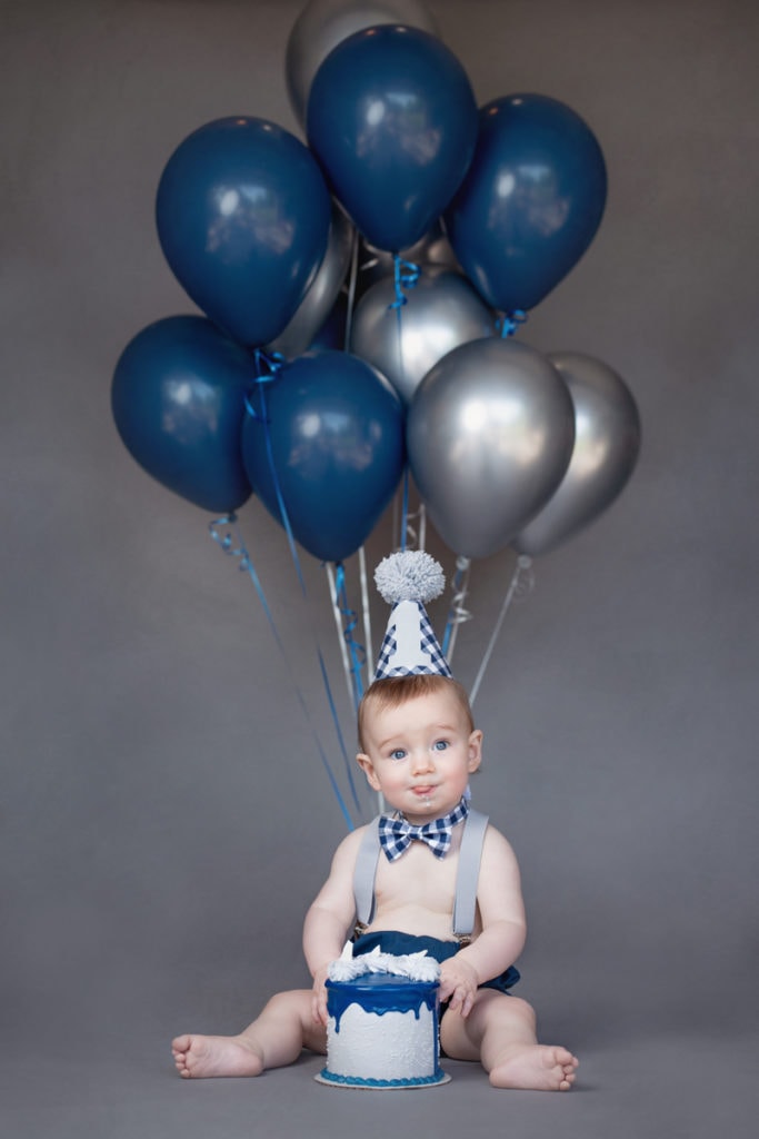 Newborn Photographer, A baby sits with party props and a bundle of balloons attached to him