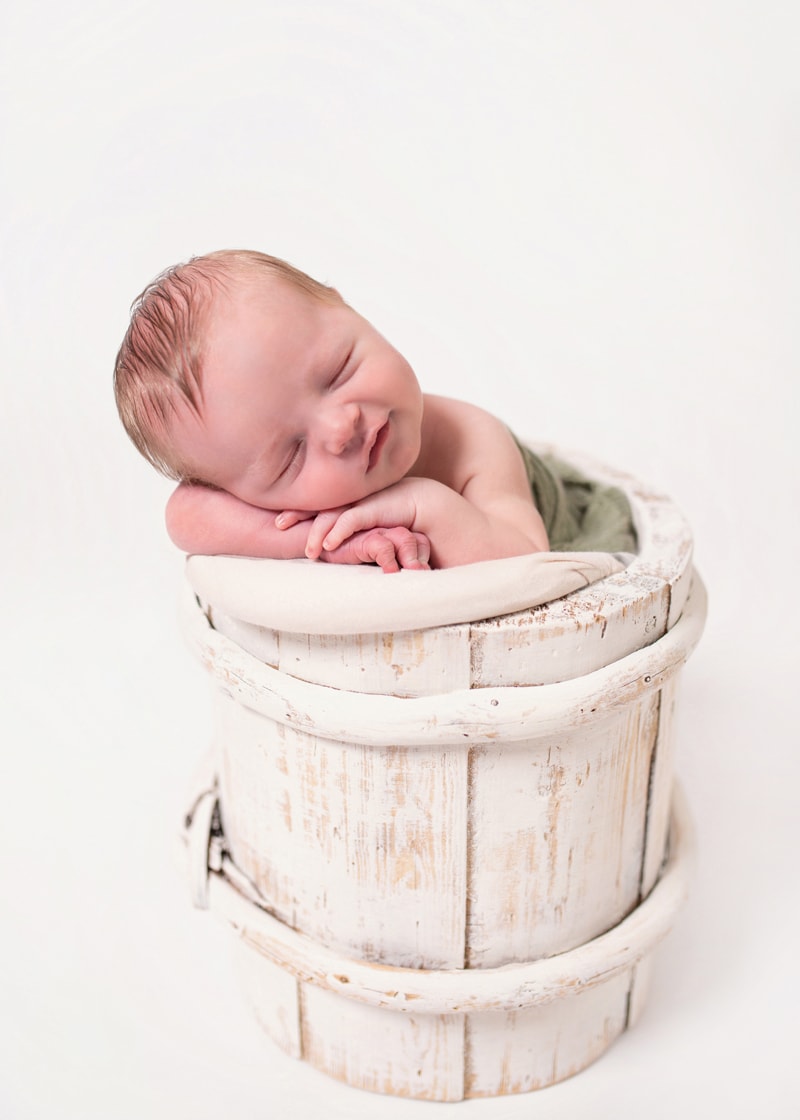 Newborn Photography, a baby sleeps on linens within a wooden bucket