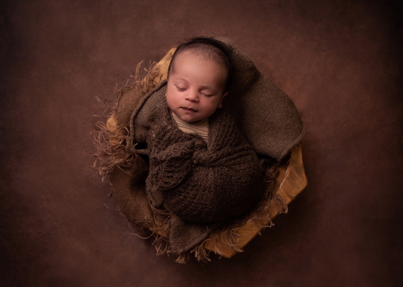 Newborn Photography, a baby lays sleeping softly in a knit blanket within a basket