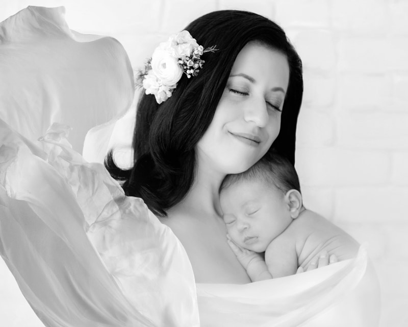 Newborn Photography, a mother with a flower in her leans into her little baby happily