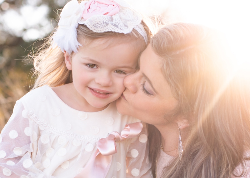 Family Photographer, mother kisses her daughter on the cheek outside