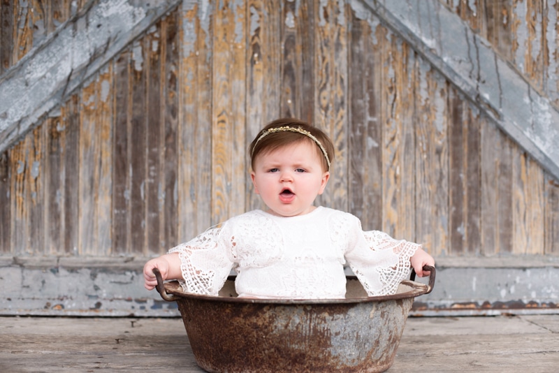 A baby girl sits in a wash bin before barn doors