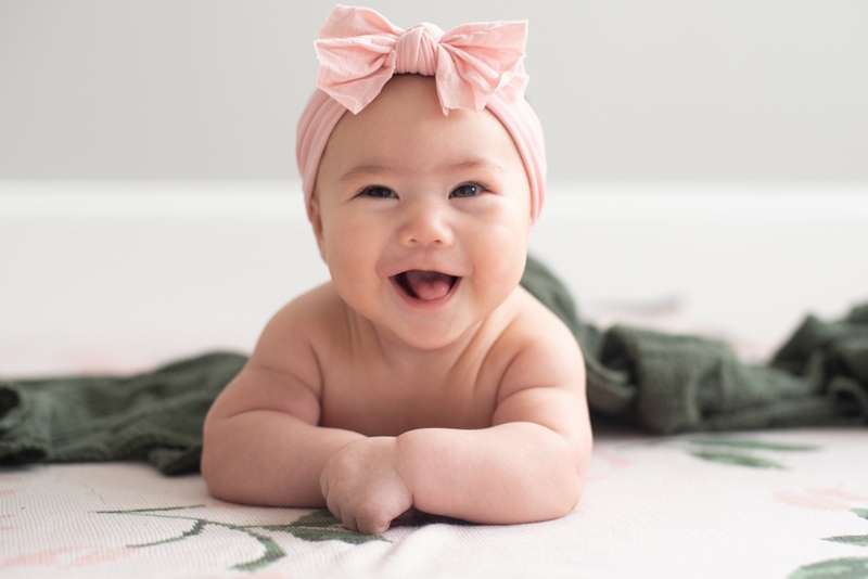 A baby girl smiles, she wears a pink bow on her head