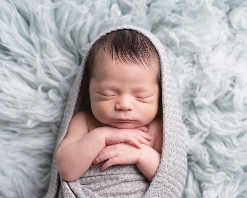 Newborn Photography, a little baby is sleeping swaddled in a blanket and on top of a cosy cushion