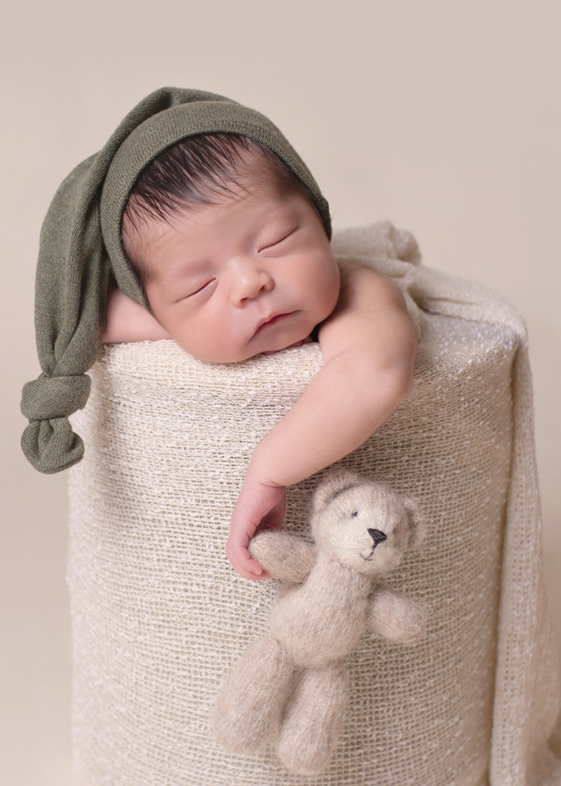 Newborn Photography, a.little baby sleeps on a cushion holding teddy bear in hand
