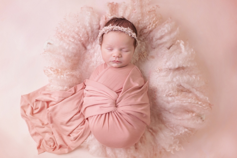 Newborn Photography, a baby girl is swaddled in a pink blanket on a fluffy pink pillow