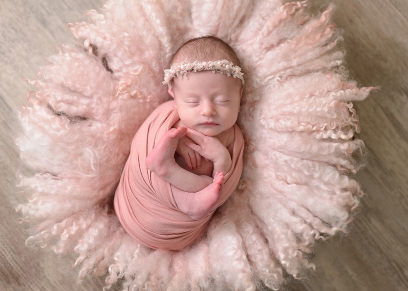 a baby lays sleeping in a fluffy bassinet, she is wrapped in pink linens
