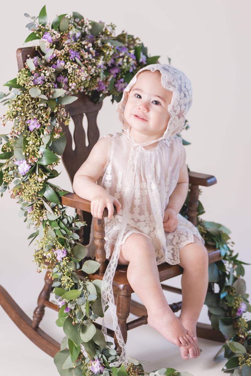 milestone photography,  a baby girl sits in a rocking chair covered with leaves and flowers