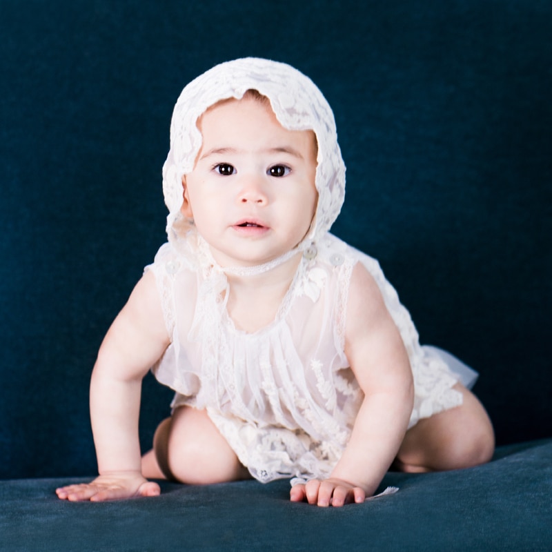 milestone photography, baby girl sits up on the couch, she wears a bonnet