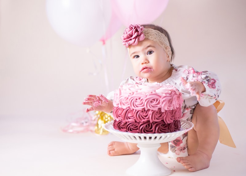 A baby girl sits before a cake decorated with flowers