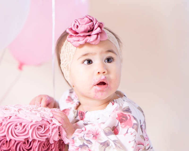 milestone photography, a little girl with a rose shaped bow on her head eats from a cake decorated with rose frosting