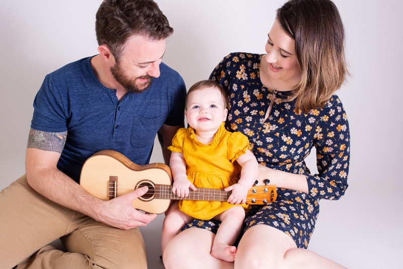 milestone photography, a mother holds their baby girl as dad leans in with ukulele