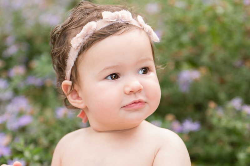 milestone photography,  a little girl with decorative headband sits outside in the garden