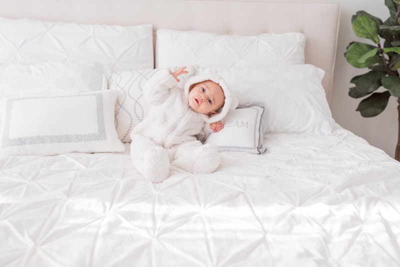 milestone photography, a young baby in a warm outfit with bear ears, plays on the bed