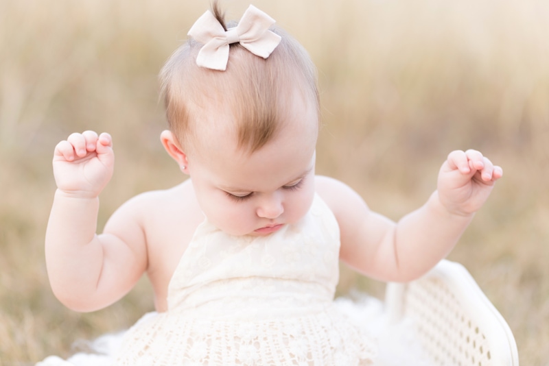 Newborn Photography, a baby girl looks at her white dress, she has a bow in her hair