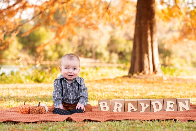 milestone photography, a baby boy sits on a picnic blanket in the park with blocks beside him that read 'Brayden'