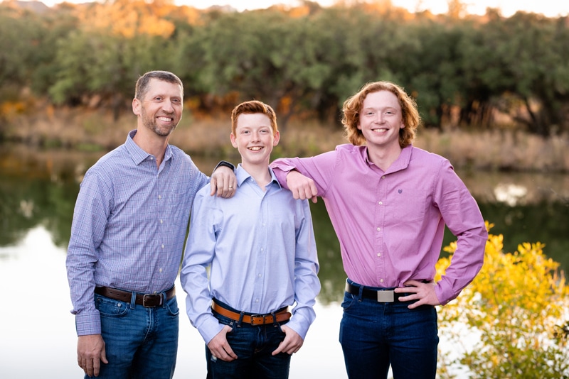 Family Photographer, dad stands tall and proud with his two sons near the lake