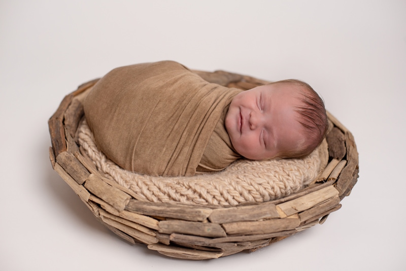Newborn Photography, a smiling baby lays swaddled in basket