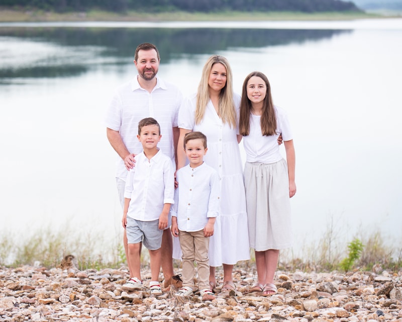 Family Photographer, a young family of 5 stand on the lakeshore's edge