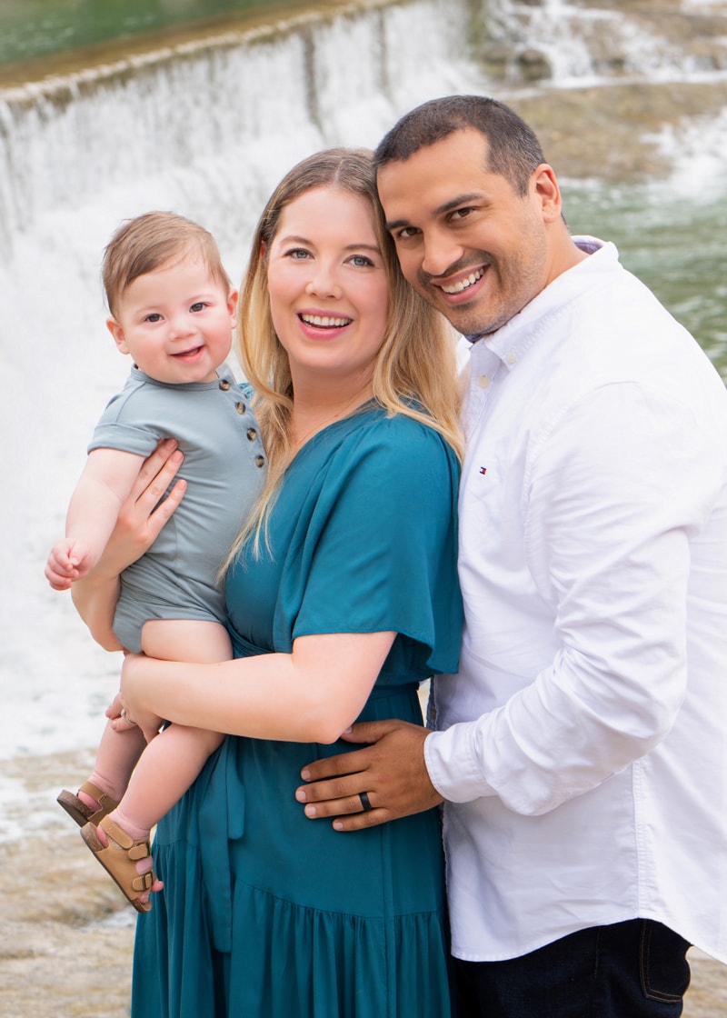 Family Photographer, Young father and mother stand near a waterfall with their happy baby