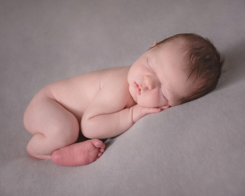 Newborn Photography, a baby lays sleeping on a cushion