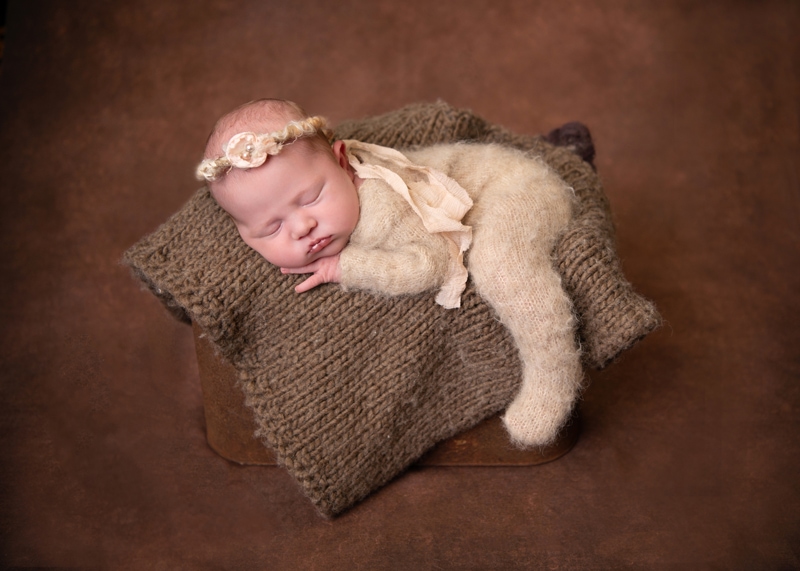 Newborn Photography, a baby sleeps on a cosy knit blanket propped over a wooden box in the studio