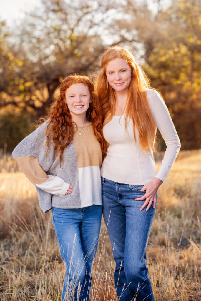 About Photographer Kelli, She is a mother and stands with her daughter in dry grassy field